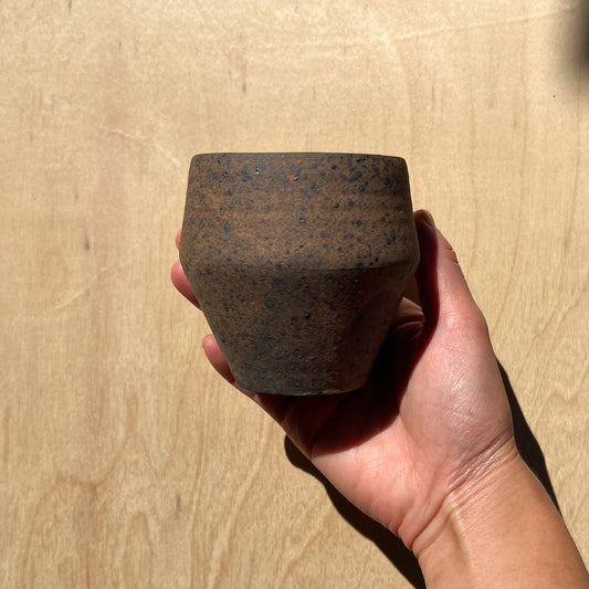 rustic beveled tea cup held in a hand against a wooden backdrop